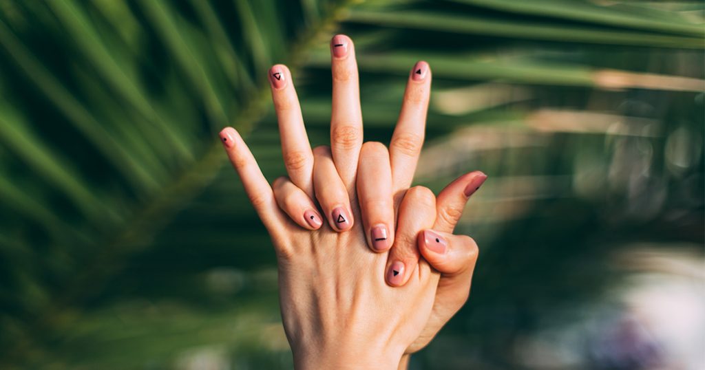 Una persona con las uñas pintadas sujetándose las manos.