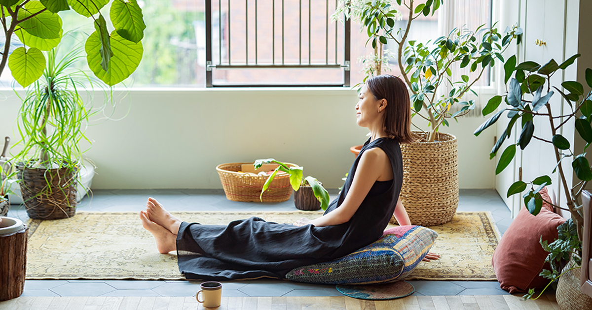 A woman sitting on the floor enjoying a quiet moment surrounded by plants.