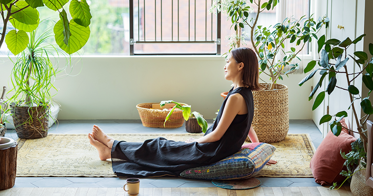 Una mujer sentada en el suelo disfruta de un momento de tranquilidad rodeada de plantas.