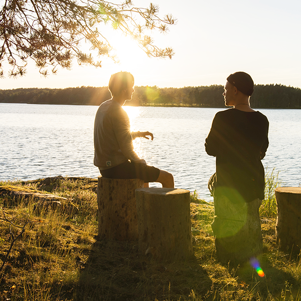 Dos hombres sentados en los tocones de un árbol junto a un lago al atardecer.