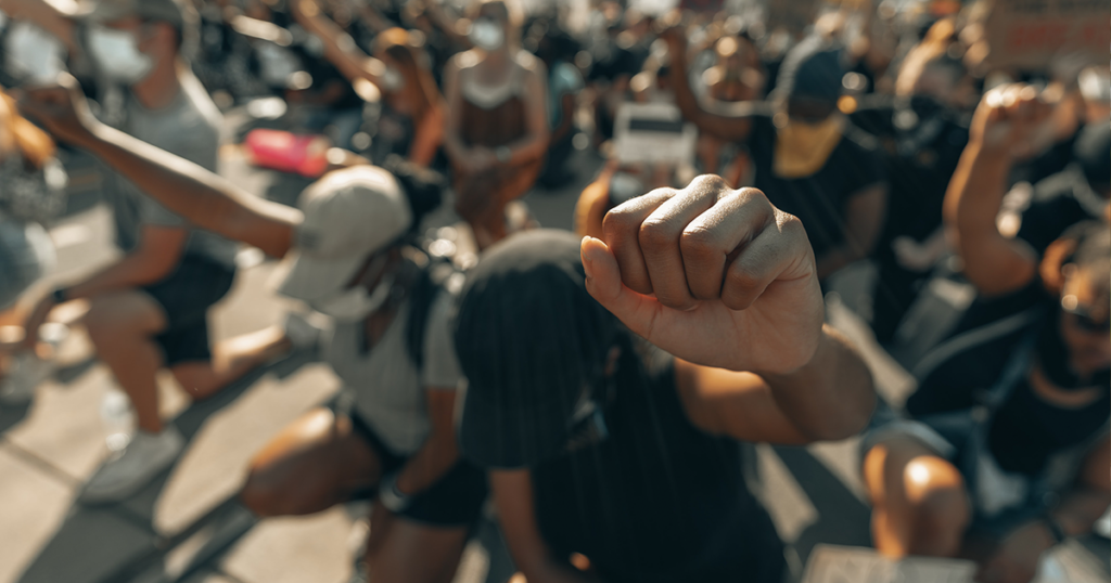 A crowd of largely Black people taking a knee with their fists in the air at a protest.