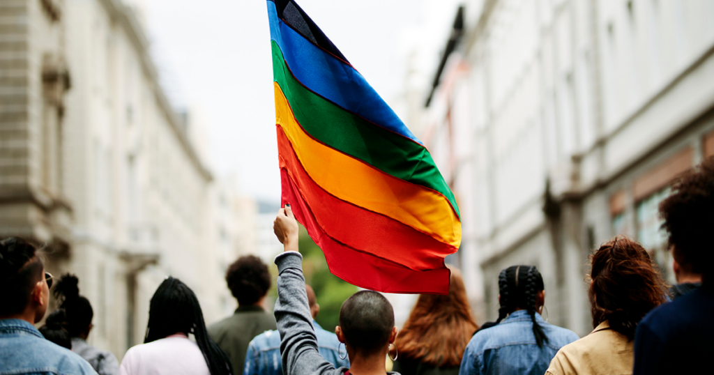 An individual walks in a crowd holding a rainbow flag above their head.