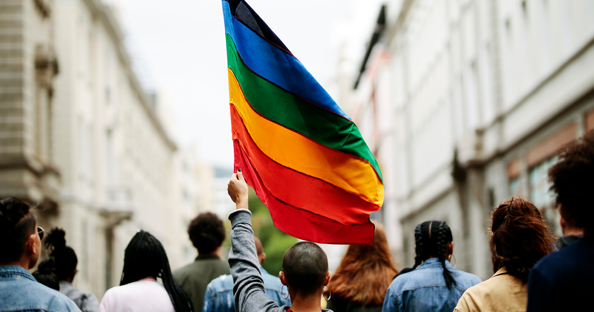 An individual walks in a crowd holding a rainbow flag above their head.