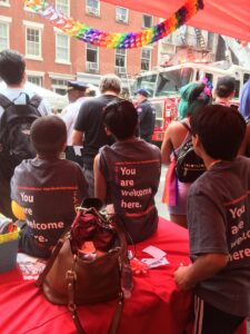The backs of three children wearing "You are welcome here" shirts at a Pride parade.