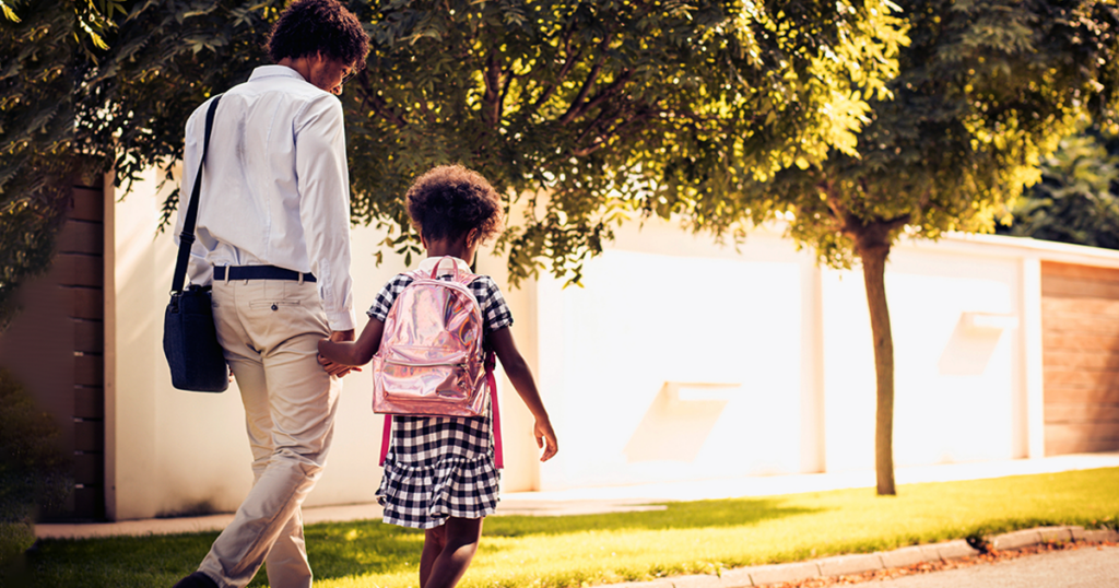 A father walks his daughter to school while holding her hand.