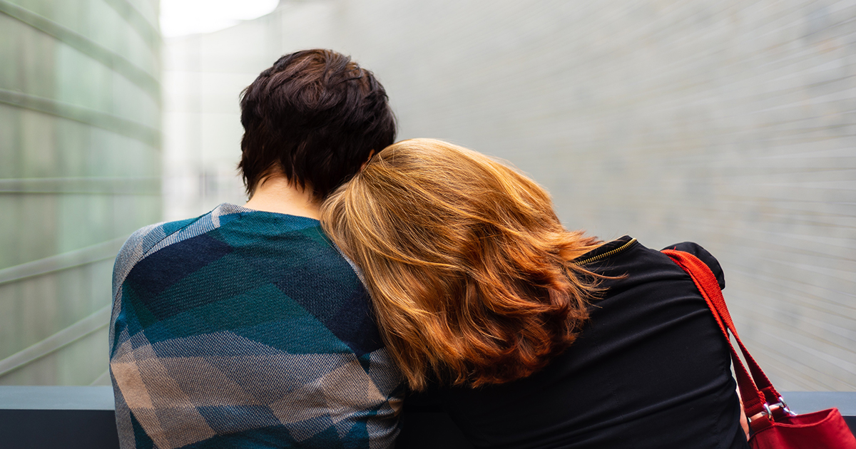 Una mujer apoya la cabeza en el hombro de una amiga.