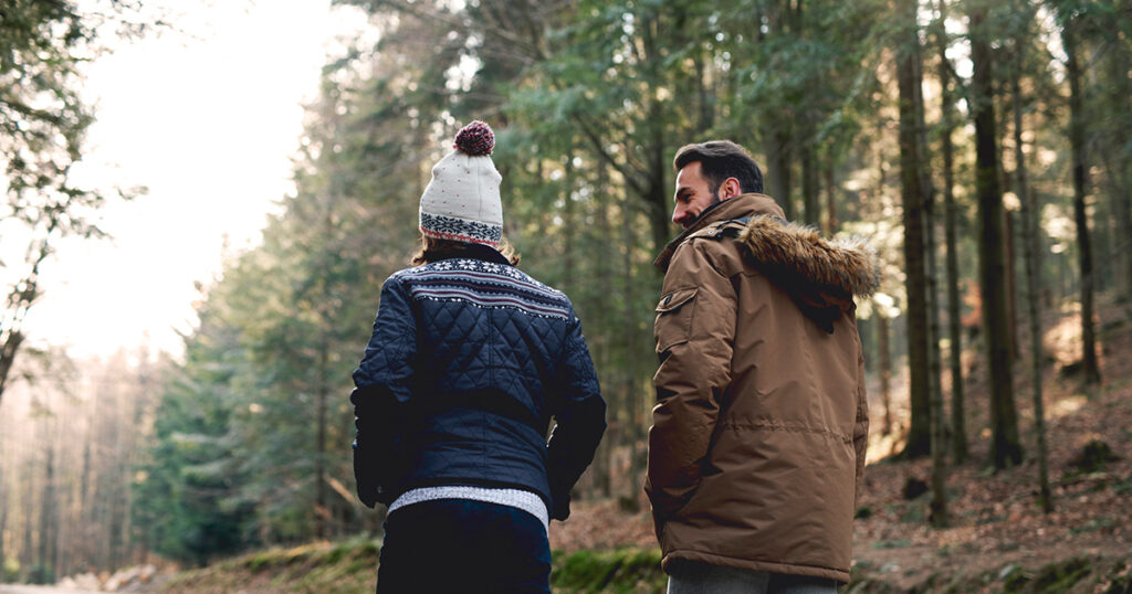 A man and a woman in winter jackets walk along a tree-lined path.