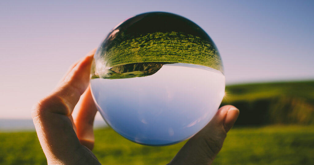 A hand holds up a glass sphere that reflects the sky and grass upside down.