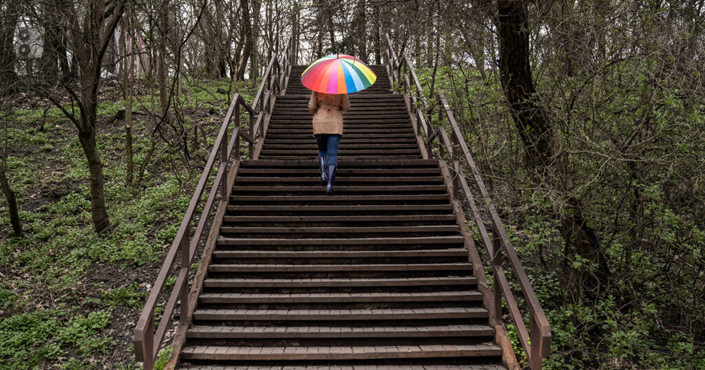 A woman walks up stairs outside holding a rainbow umbrella.