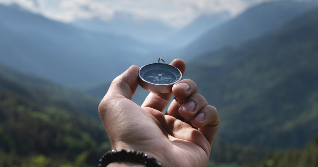 A hand holds a compass facing mountain views.