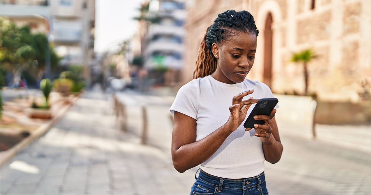 A woman stands on a city street using her phone.