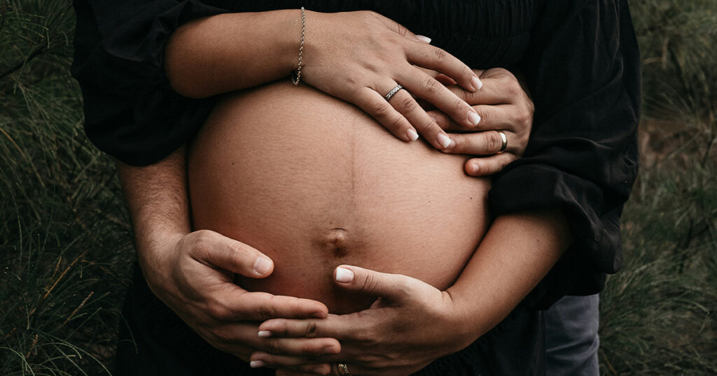 Two pairs of hands cradle a pregnant belly.
