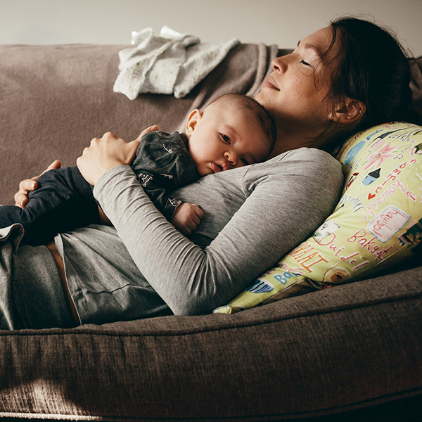 A woman with closed eyes lays on the couch with her new baby