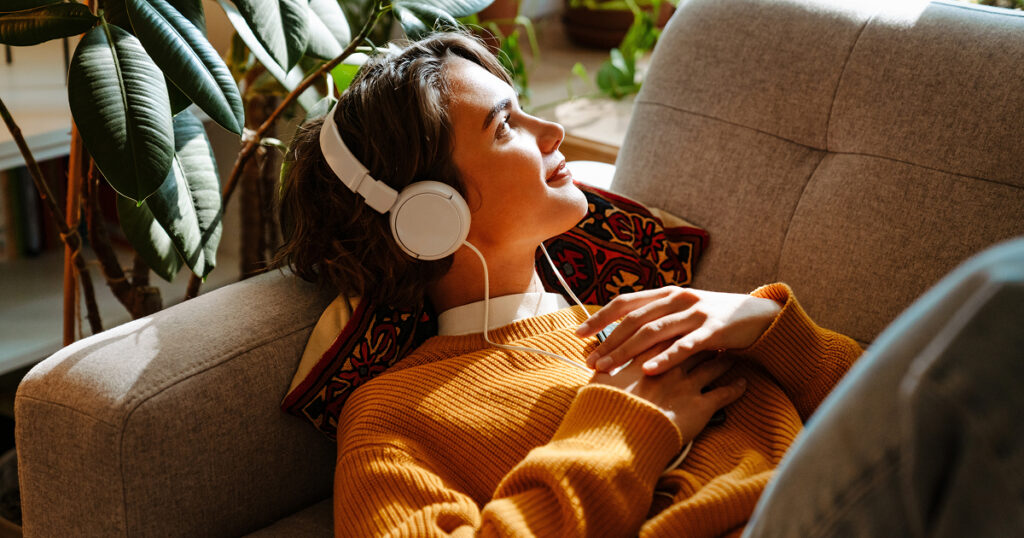 A woman lounges on a couch wearing headphones.