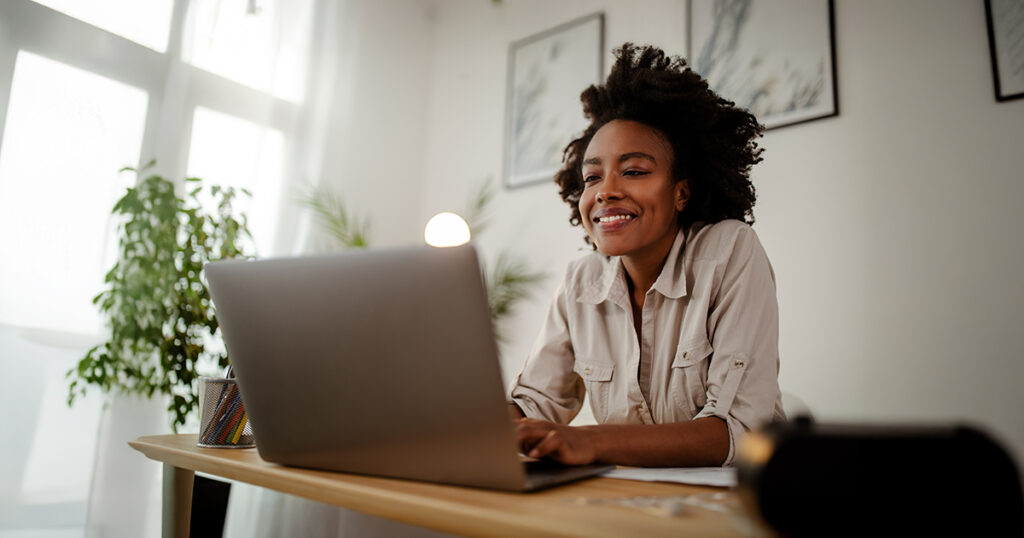 A woman sits at a table and looks at a laptop.