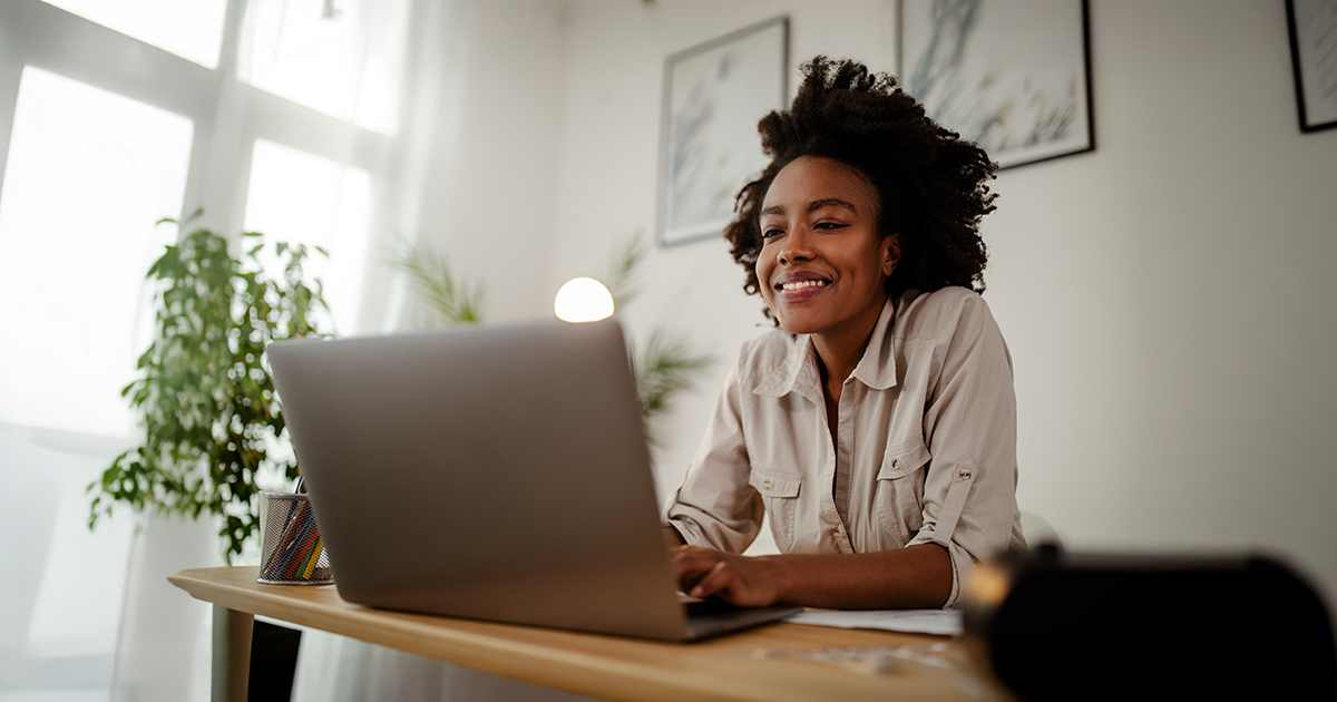 A woman sits at a table and looks at a laptop.