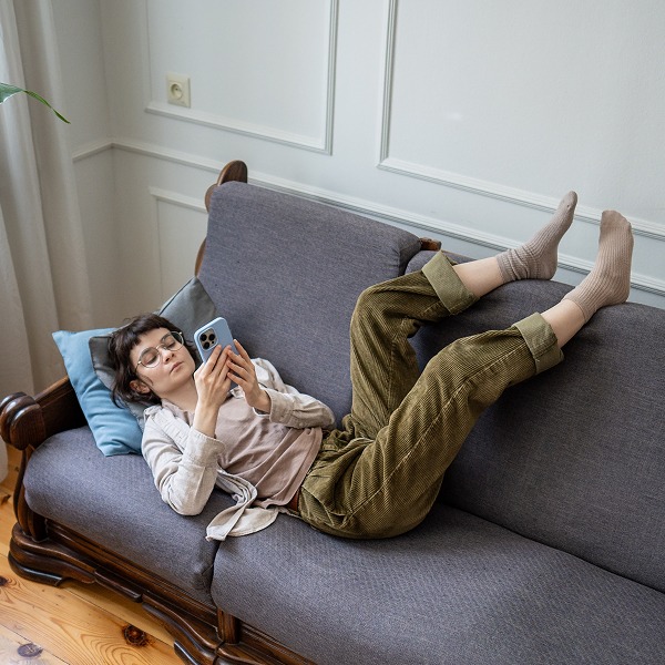 5 ways to break the procrastination cycle_600x600 A woman looks at her phone while laying on the couch with her feet up against the back cushions.