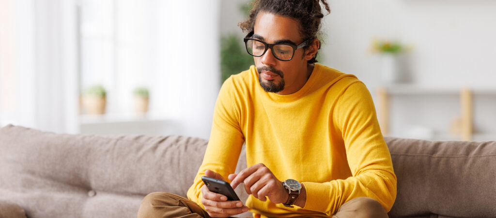 A man sitting on a couch touches his phone screen.